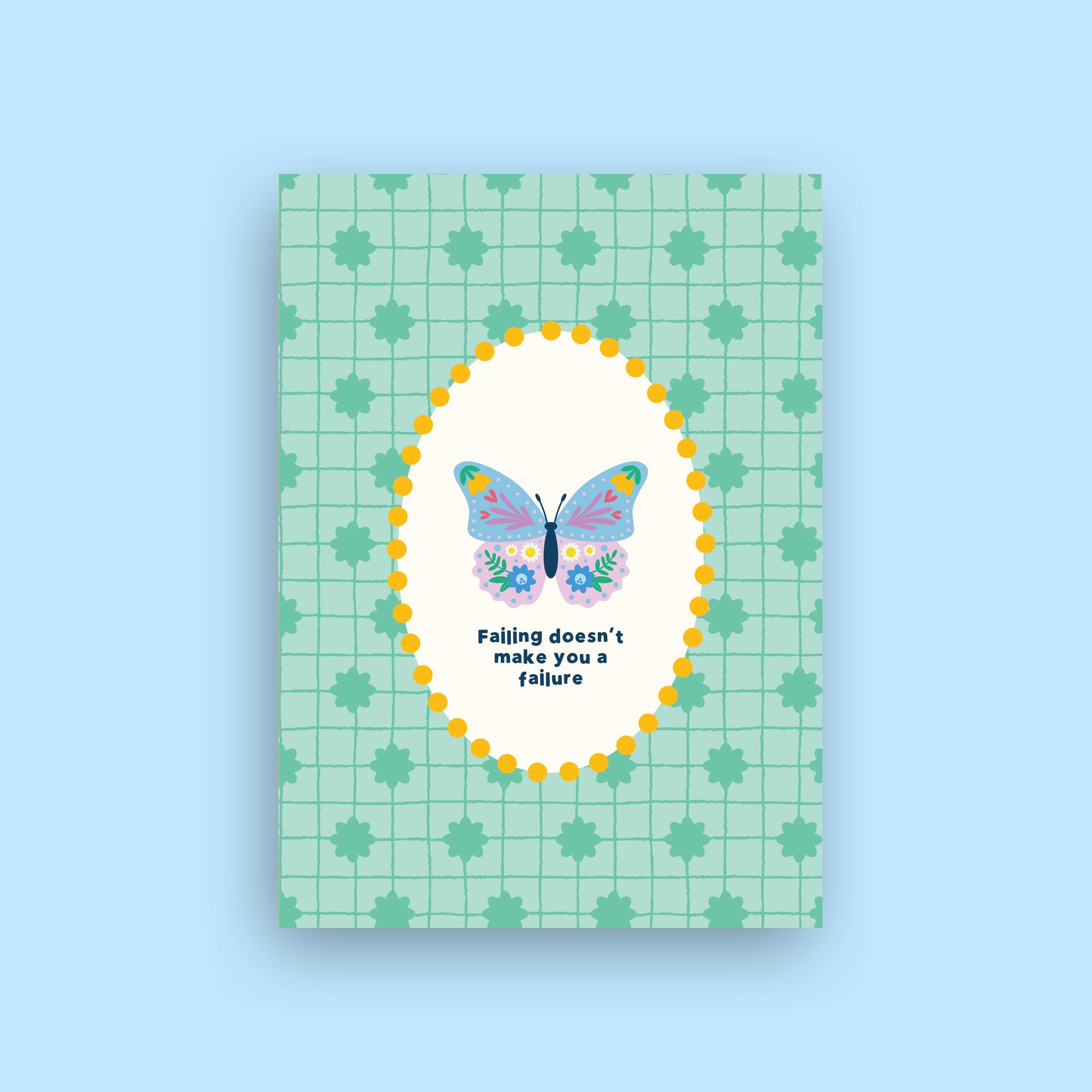 A rectangular greeting card with a mint green grid and leaf pattern, featuring a central white oval with a colorful butterfly and the text 'Falling doesn't make you a failure'. The card is shown against a solid light blue background.