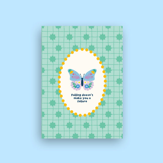 A rectangular greeting card with a mint green grid and leaf pattern, featuring a central white oval with a colorful butterfly and the text 'Falling doesn't make you a failure'. The card is shown against a solid light blue background.